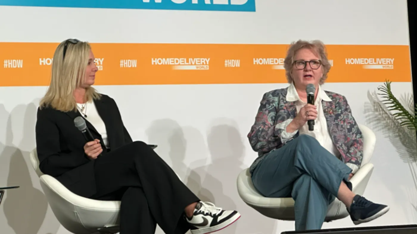 Two people are seated on a conference stage.