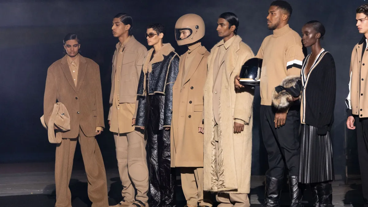 Models in brown clothing line up on a darkened runway.