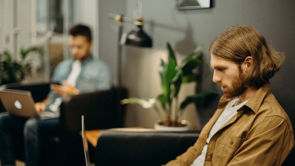 Side profile: a White man with long hair and a beard works on a laptop