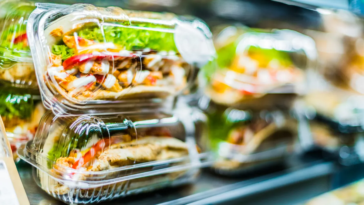 Plastic takeout containers with chicken sandwiches in a commercial refrigerator