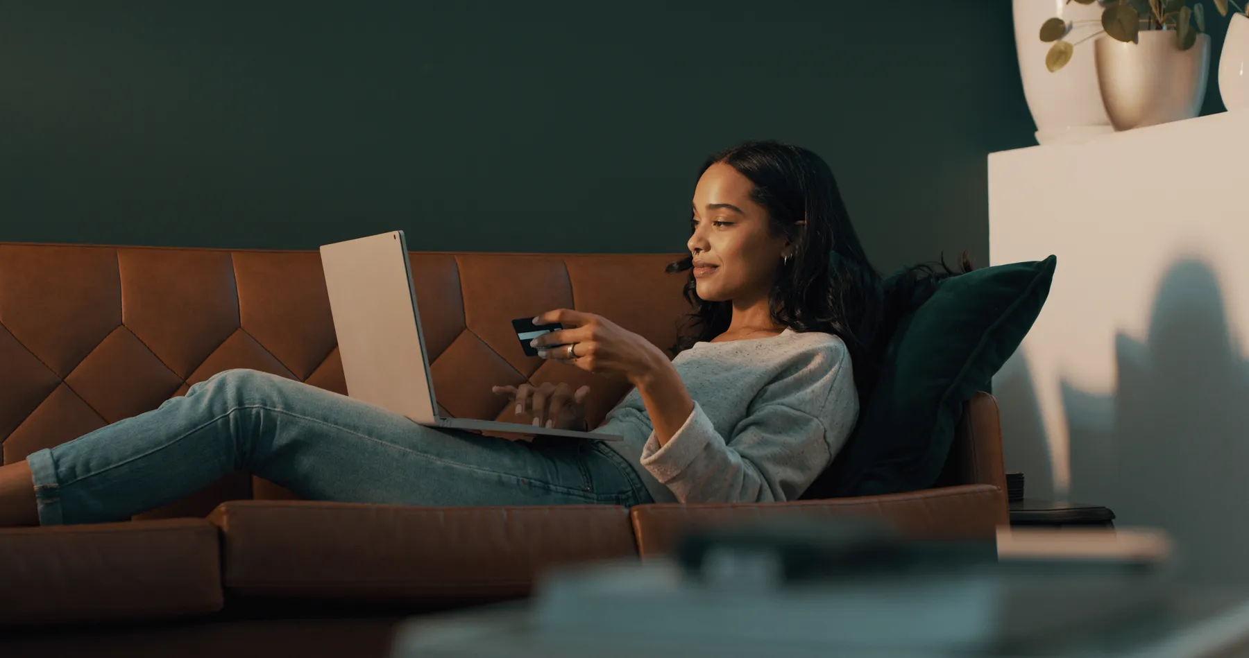 Person laying back on a couch with a computer and a credit card shopping.