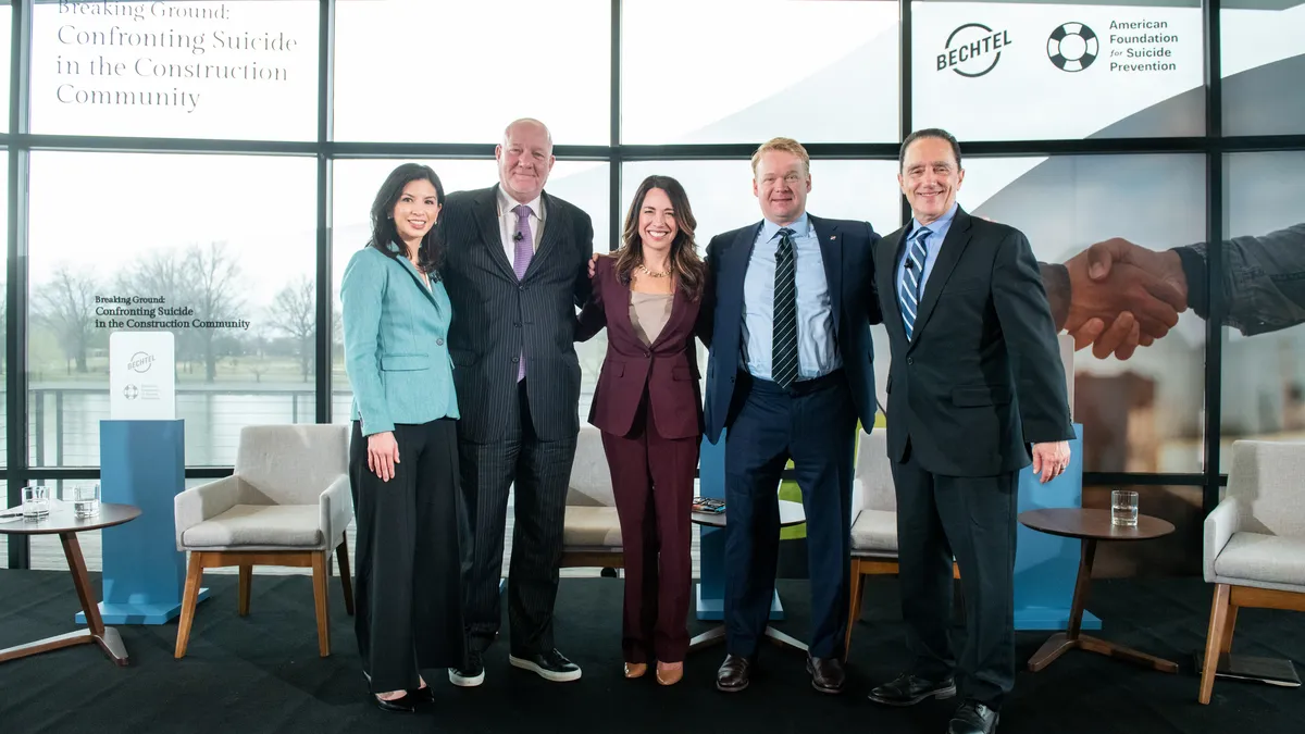 A group of five people pose on a small stage for a photo.