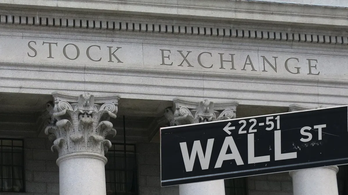 Sign reads "wall street" with "stock exchange" engraved on a building in the background.