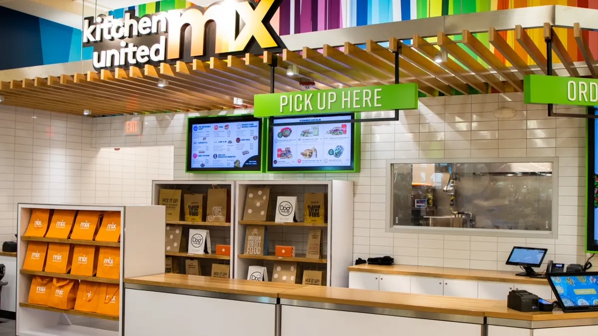 Image of a counter with a ordering kiosk and shelves in the background with bags.