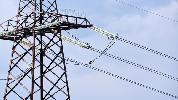 An electric transmission tower stands against a blue sky.