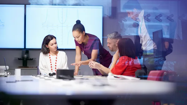 Meeting room scene where a woman is speaking infront of screen