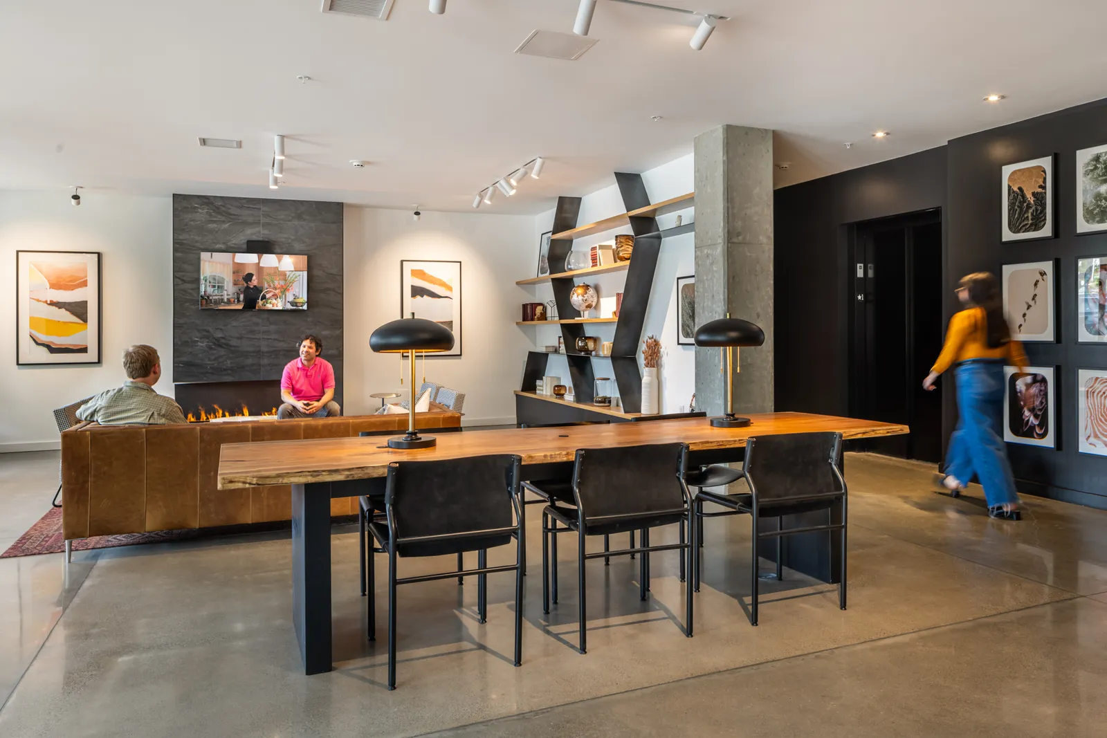 A room with couches, tables, and a fireplace. Two people are sitting at the couches.