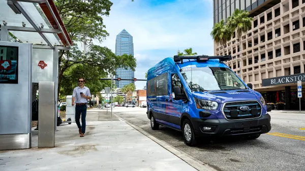 Man walking on sidewalk near a bus shelter with a blue van parked on the street.