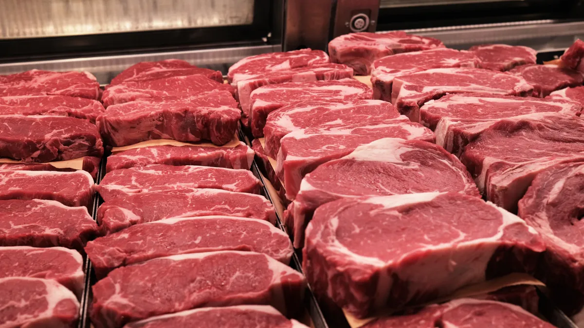 Raw steaks are seen from the perspective of inside a deli case.