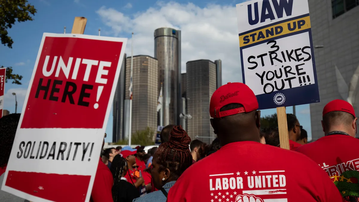 UAW union members strike holding signs with the city in the background.