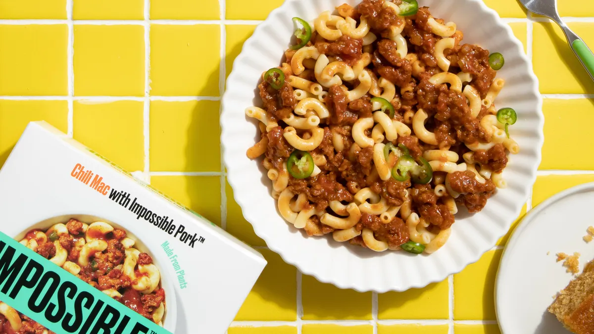 Impossible Foods' Chili Mac on a white plate, sitting on a yellow tiled countertop with the branded box in the lower left corner.