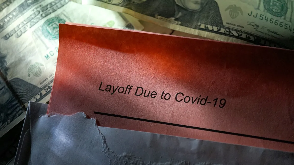 A letter containing a COVID-19 layoff notice is opened against a backdrop of U.S. dollar bills.