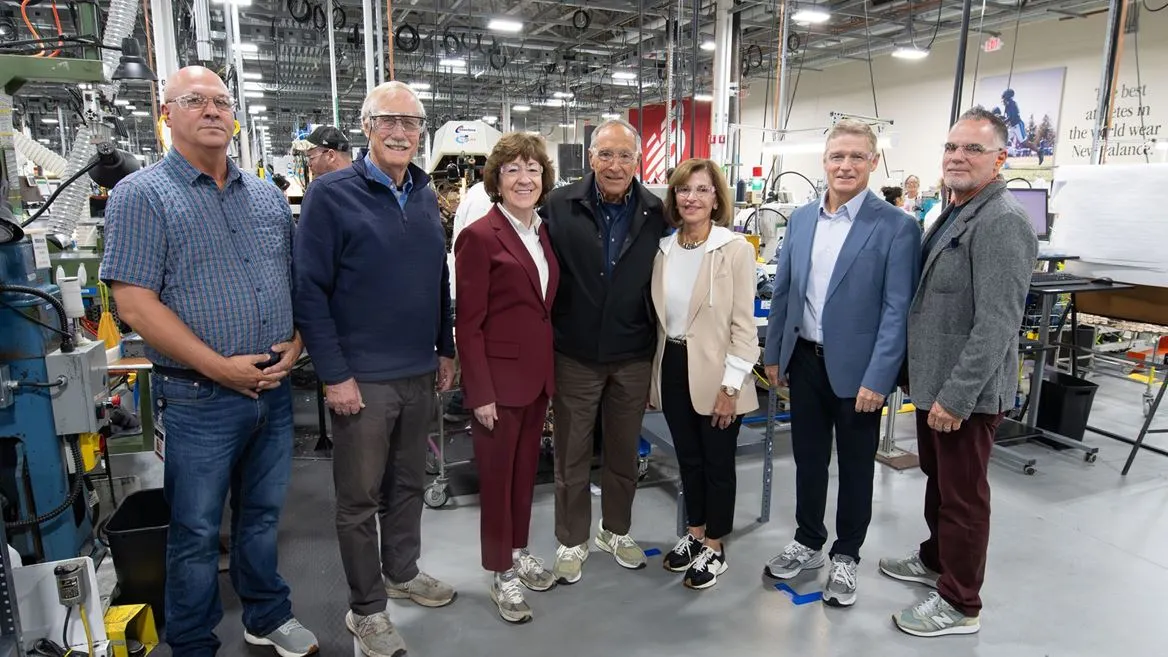 A group of people, some wearing safety glasses, stand in a footwear manufacturing facility
