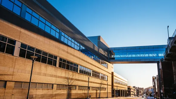 A hospital skyway over a street between two buildings appears against a clear blue sky on a snowy day.