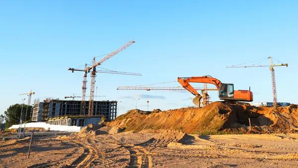 Large cranes tower over dirt and construction machinery on a jobsite.