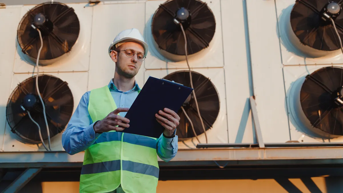 A technician looks at a work order form in front of a industrial HVAC units.