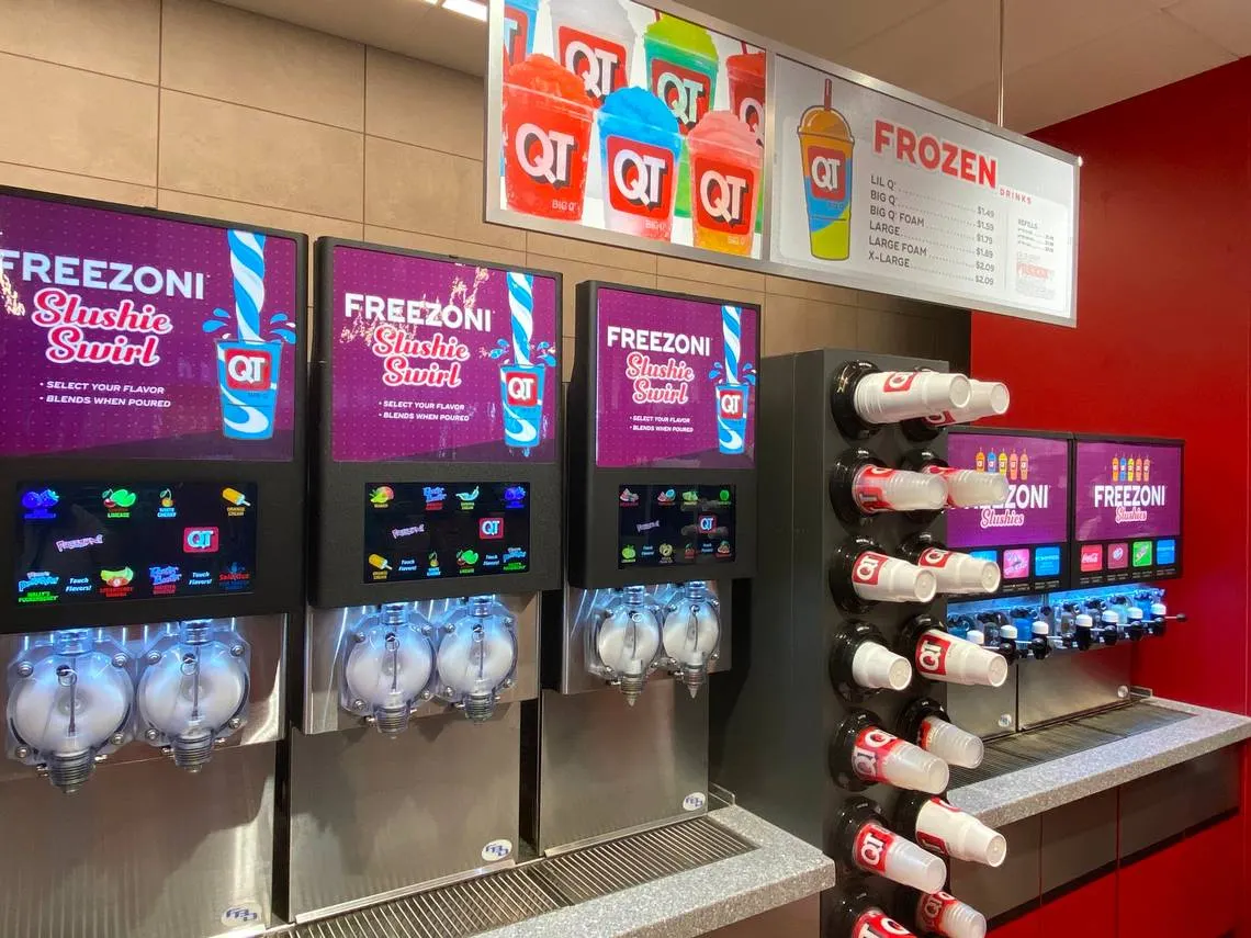 A photo of a bank of frozen drink dispensers. The signs on the machines say Freezoni Slushie Swirl, while a menu above the machines says Frozen.
