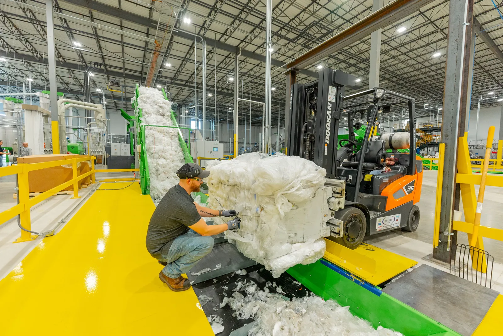 A person working on industrial machinery to create bales of plastic film.