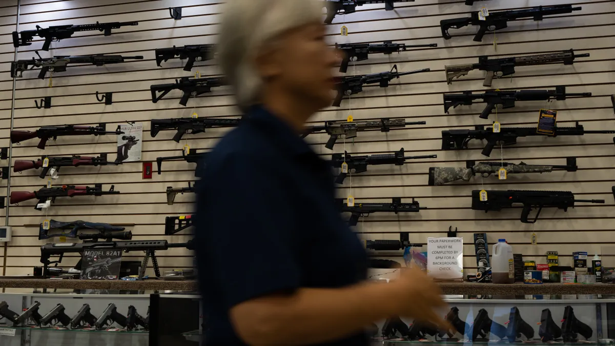 Guns are shown in a gun store as a person passes by