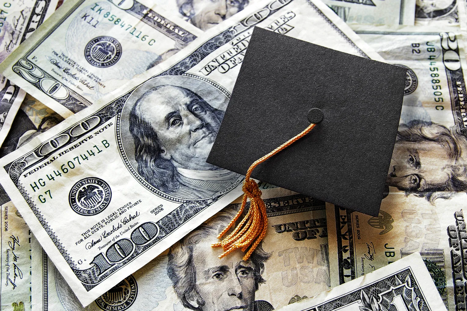 A small graduation cap sits on a pile of money.