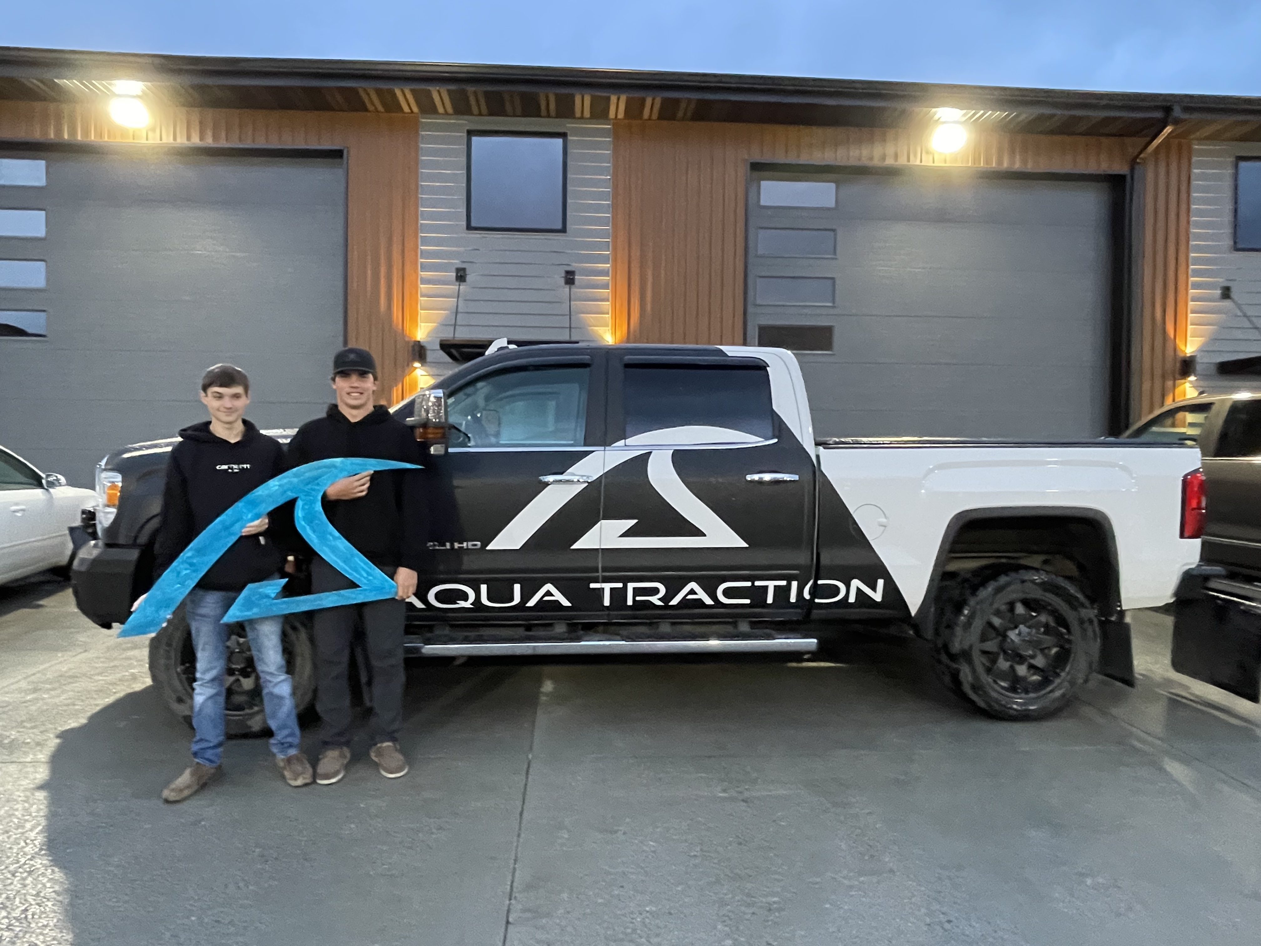 Two boy students stand next to a white and black pickup truck that they have outfitted with signage for a local business in Bismarck, North Dakota.