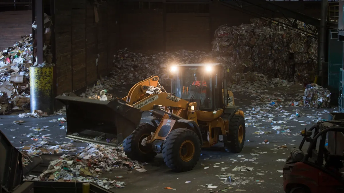 A bulldozer moves piles of paper at a recycling facility