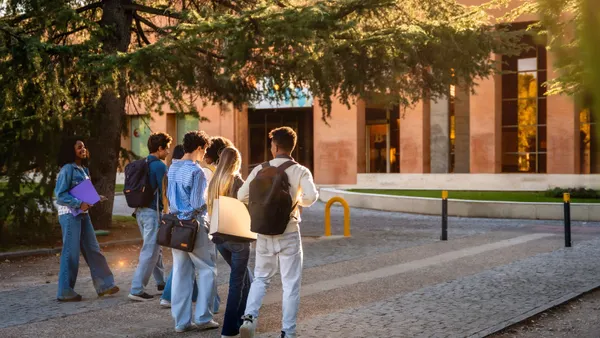 A group of college students walk on a sidewalk on a college campus.