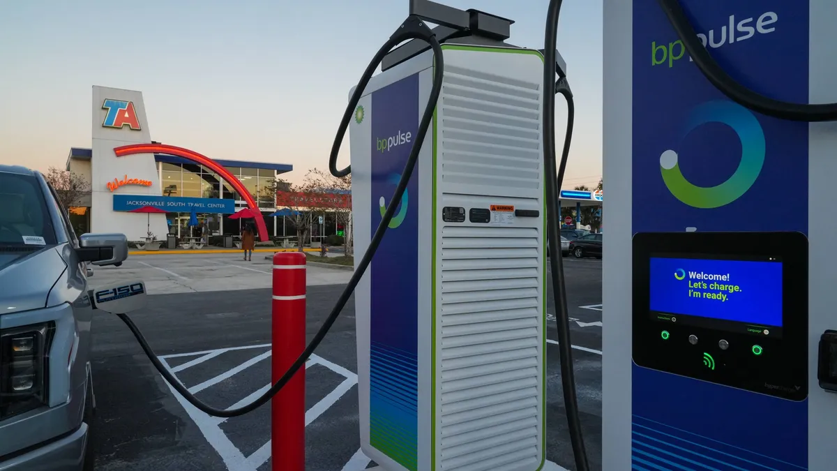 A photo of an electric vehicle charging at a charging station. the charger says "BP Pulse" on the front. A convenience store is in the background, with a sign over the door that says "TA Welcome Jacksonville South travel center."