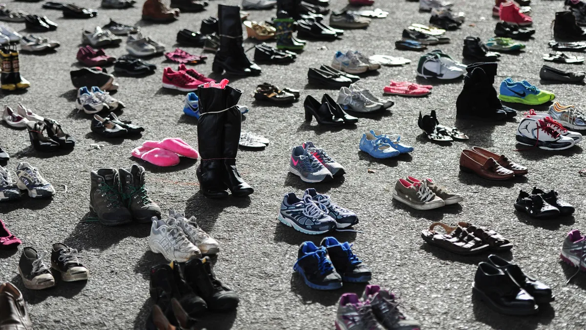 Pairs of empty shoes and boots on pavement.