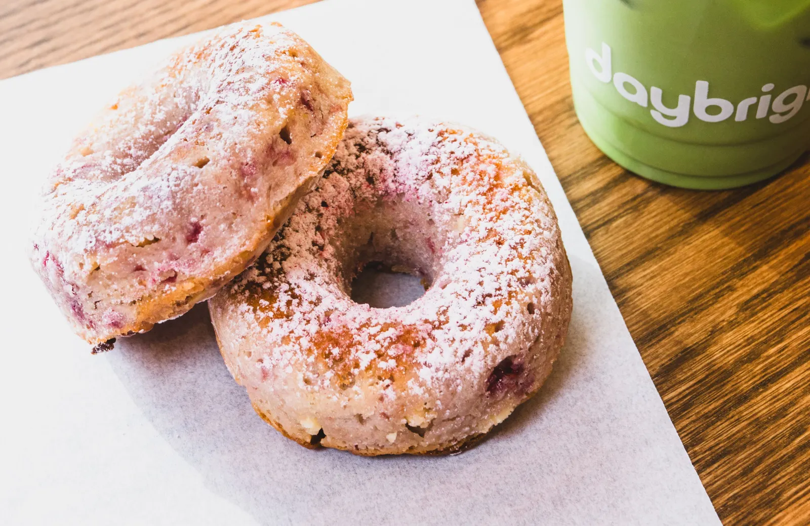 Two donuts on a white napkin with a green drink on the right side.