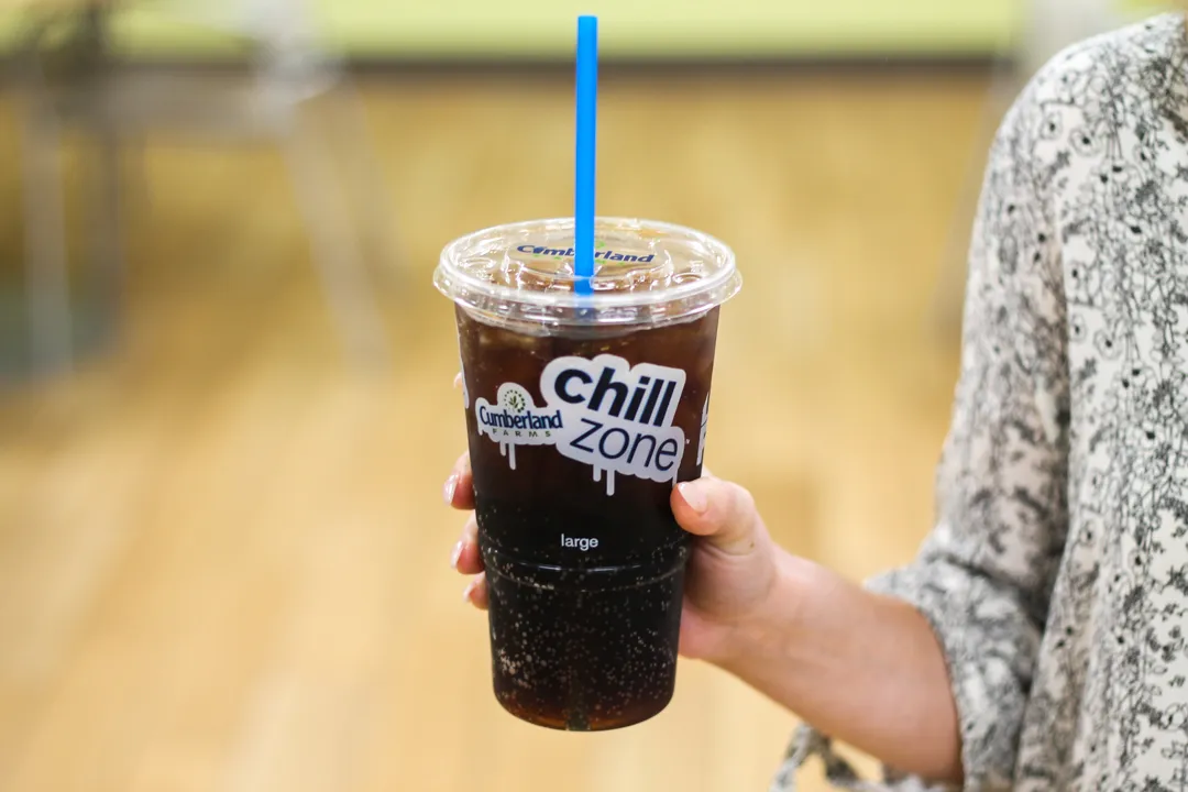 A photo of a hand holding a disposable clear cup with soda inside and a straw through the lid. The cup says Cumberland Farms Chill Zone.