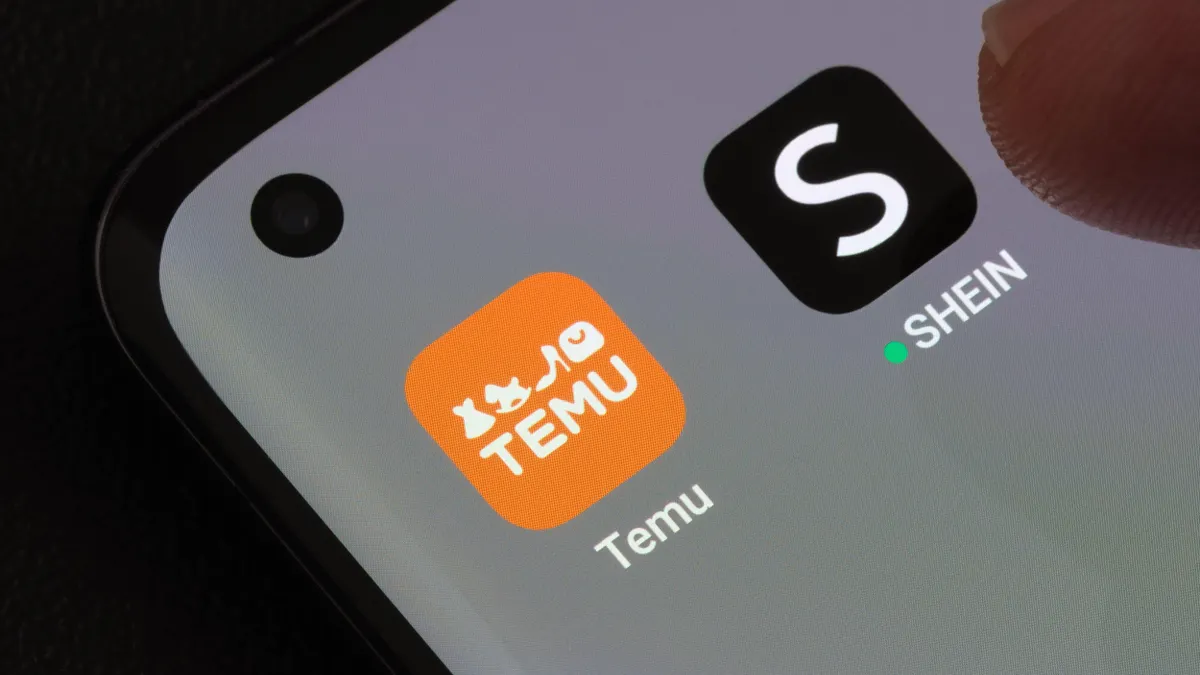 Close-up of a smartphone screen displaying the Temu and Shein shopping apps, showcasing a finger tapping the Sein app. 