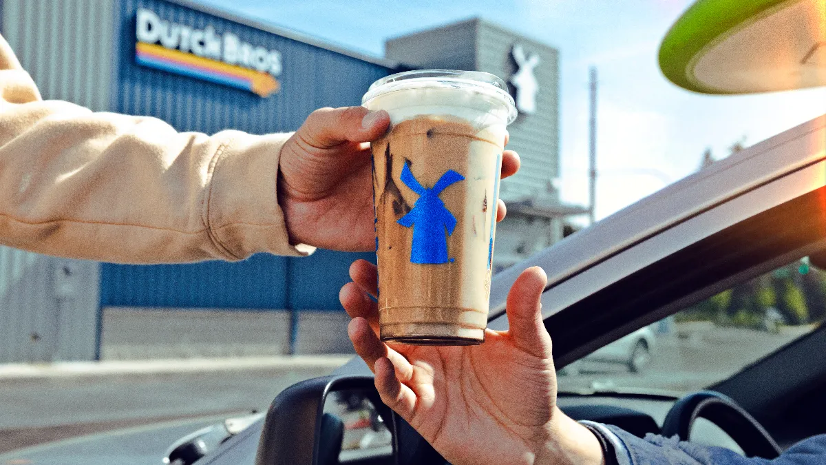 A picture of a hand giving a iced coffee drink to another person.