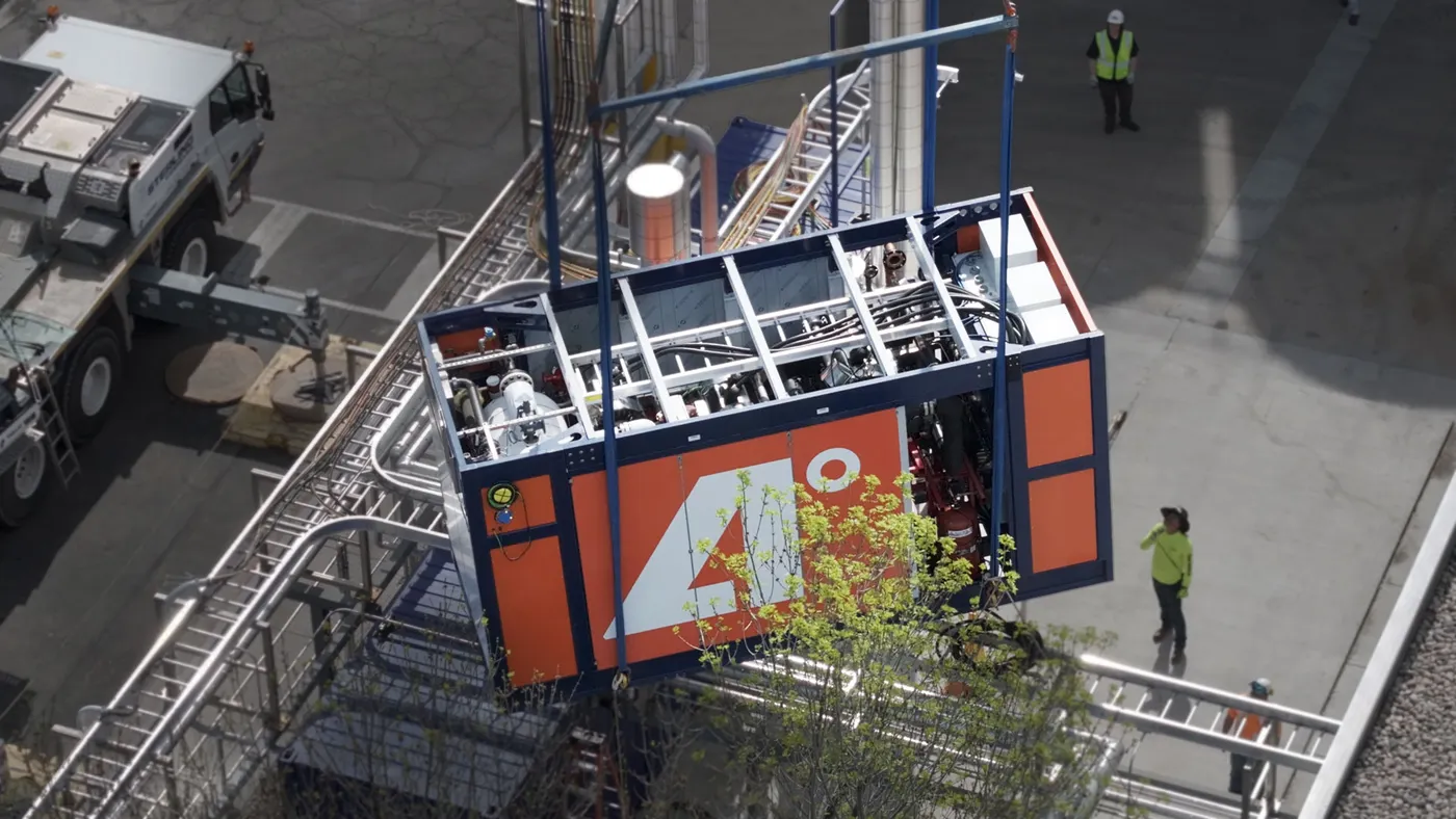 A piece of industrial equipment is lowered into place, with workers on the side