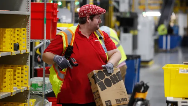 An Amazon warehouse employee wearing a festive hat scans a package.