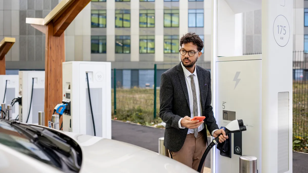 A wide-angle side view of a man in business dress stood at an electric charging station