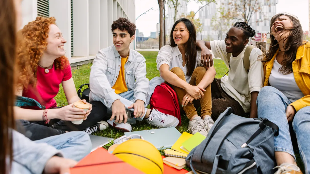 A diverse group of college students sitting on the grass outside a modern campus building.