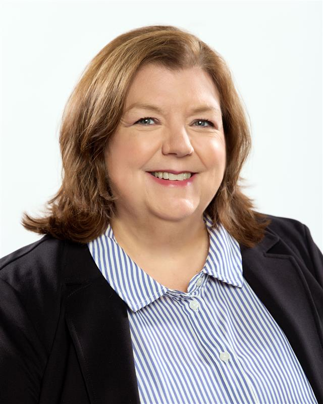 A smiling person with brown hair wearing a striped shirt and dark blazer.