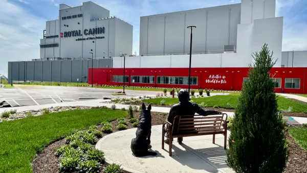 Statues of a person and a dog facing a gray and red factory.