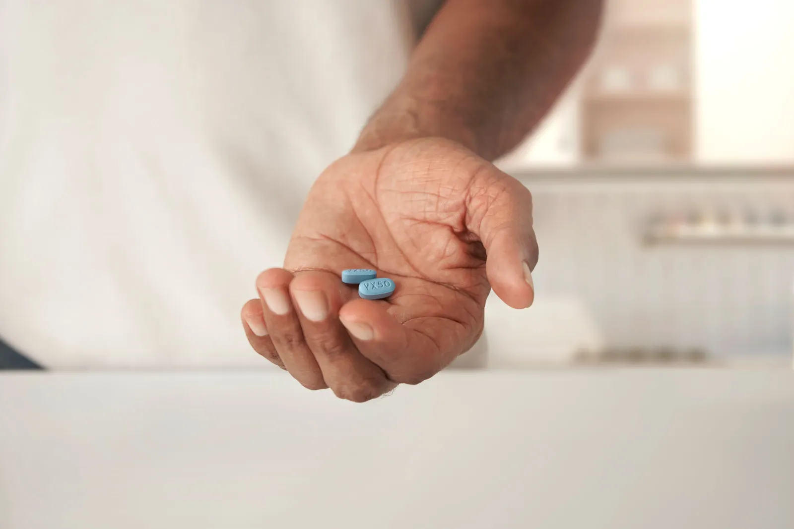 A person holds two blue drug tablets in their left hand.
