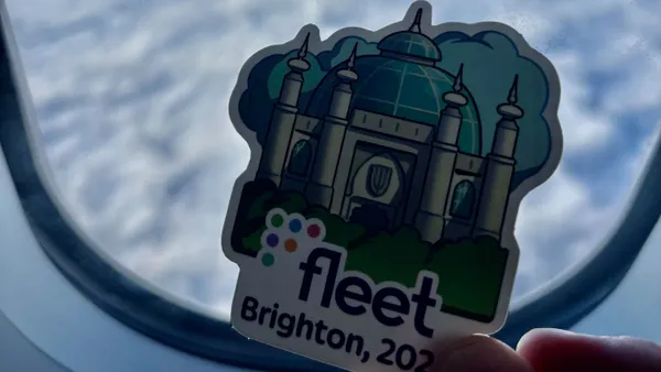 A sticker with technology device management firm Fleet's logo is pictured in the hand of the person seated in an airplace.