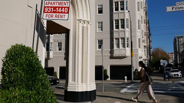 An apartment for rent sign hangs outside of an apartment building.