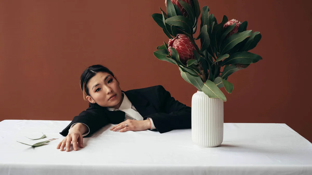 An Asian person is tired at their desk; there are flowers on the desk