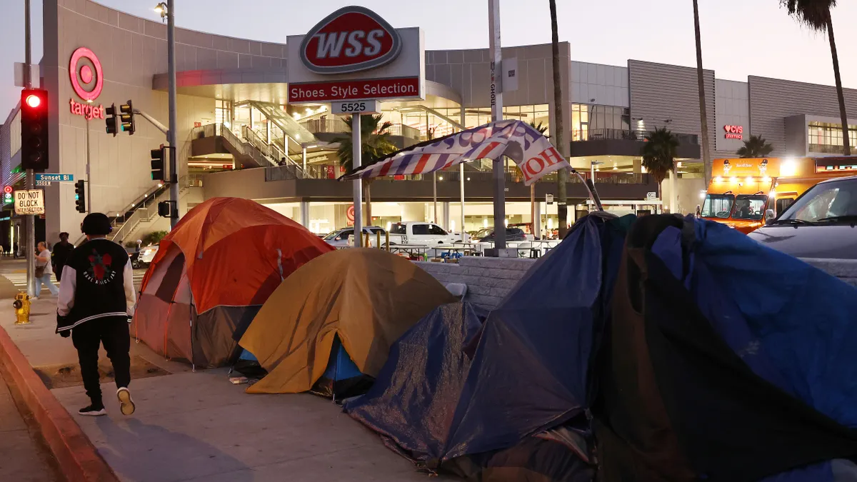 A person walks by tents lined up on the sidewalk in front of stores.