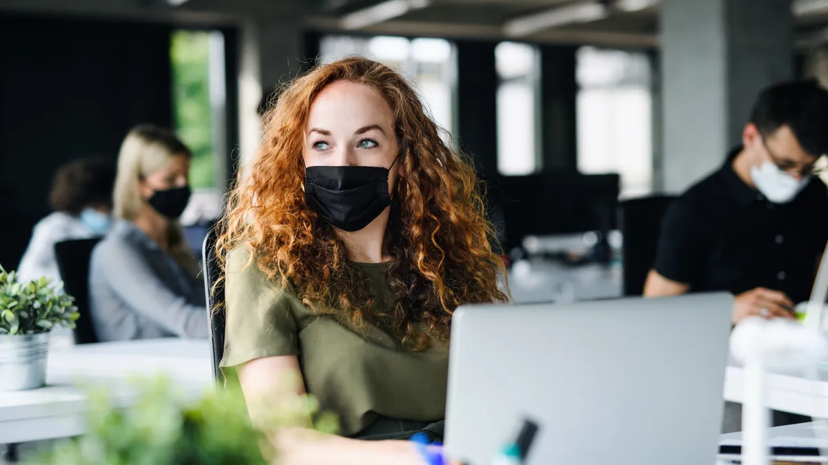 woman using computer in library or office while wearing a facemask