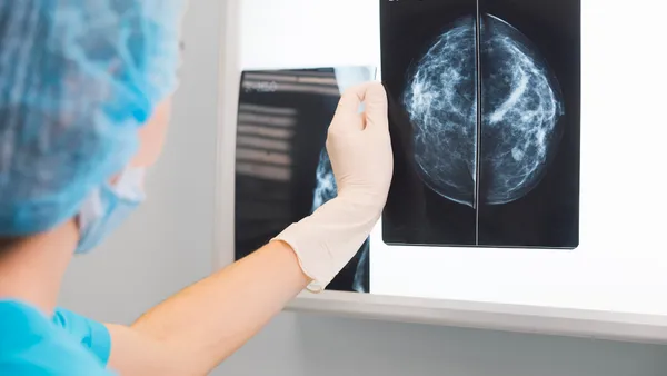 A person in scrubs and gloves holds an image of a mammogram above a lighted panel