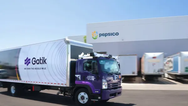 An purple autonomous truck with the Gatik logo on the trailer drives by a PepsiCo facility.