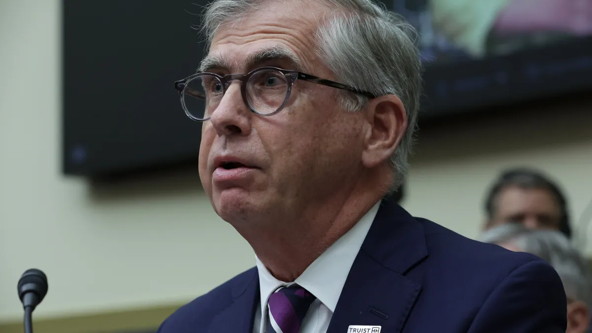 Truist CEO Bill Rogers, wearing a suit and sitting near a microphone, speaks during a Congressional hearing