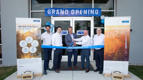 Five people stand in front of a Nefab building with a grand opening sign and get ready to cut a giant ribbon.