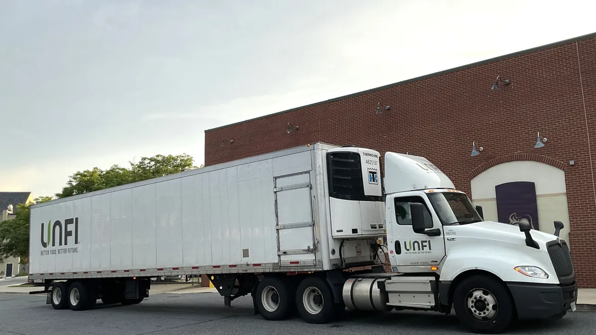 A white tractor-trailer in front of a red brick building.